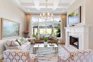 Living room featuring beamed ceiling, coffered ceiling, an inviting chandelier, a fireplace, and white oak floors