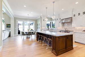 Kitchen with wall chimney exhaust hood, plenty of natural light, and white cabinets