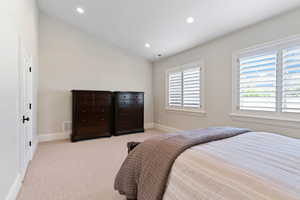 Bedroom with light carpet, vaulted ceiling, and multiple windows