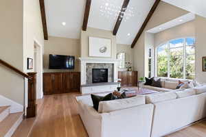 Living room with white oak floors, beamed ceiling, high vaulted ceiling, and a stone fireplace