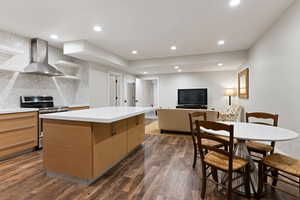 Kitchen with decorative backsplash, dark wood flooring, wall chimney exhaust hood, a kitchen island, and stainless steel range oven