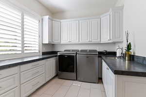 Laundry area featuring light tile patterned flooring, sink, independent washer and dryer, and cabinets