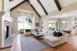 Living room with high vaulted ceiling, a fireplace, white oak floors, a notable chandelier, and plenty of natural light