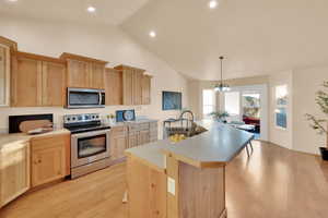 Kitchen with pendant lighting, sink, light hardwood / wood-style flooring, an island with sink, and appliances with stainless steel finishes