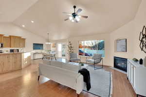 Living room with ceiling fan with notable chandelier, light hardwood / wood-style flooring, and vaulted ceiling