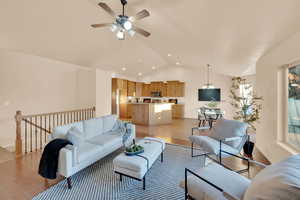 Living room featuring ceiling fan with notable chandelier, lofted ceiling, and light hardwood / wood-style flooring