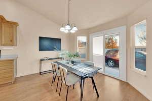 Dining space featuring plenty of natural light, an inviting chandelier, lofted ceiling, and light hardwood / wood-style flooring