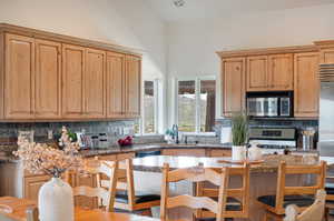 Kitchen featuring sink, backsplash, appliances with stainless steel finishes, dark stone countertops, and a towering ceiling