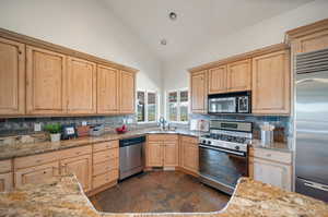 Kitchen featuring light stone counters, stainless steel appliances, sink, and high vaulted ceiling