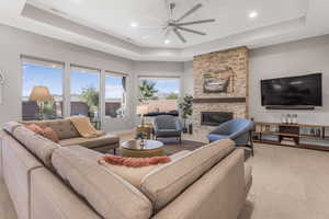 Living room featuring a raised ceiling, a stone fireplace, light tile patterned flooring, and ceiling fan