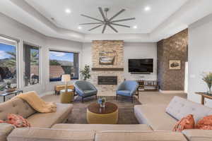 Carpeted living room featuring a raised ceiling, a large fireplace, and ceiling fan