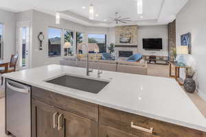 Kitchen with sink, a fireplace, a raised ceiling, decorative light fixtures, and ceiling fan