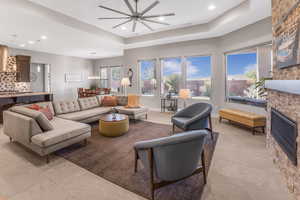 Tiled living room featuring ceiling fan, a fireplace, and a raised ceiling