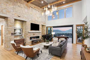 Living room featuring a stone fireplace, an inviting chandelier, a high ceiling, and wooden ceiling