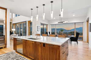 Kitchen with light wood-type flooring, a mountain view, decorative light fixtures, and a kitchen island with sink