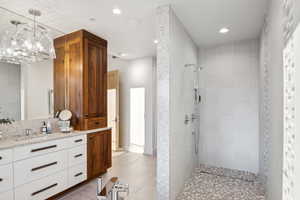 Bathroom with an inviting chandelier, vanity, a tile shower, and tile patterned floors