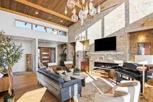 Living room featuring a stone fireplace, wood ceiling, plenty of natural light, and high vaulted ceiling