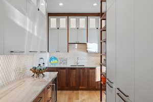 Kitchen with white cabinetry, tasteful backsplash, light stone countertops, light hardwood / wood-style flooring, and sink