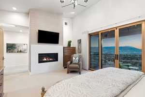 Carpeted bedroom with access to outside, high vaulted ceiling, and a large fireplace