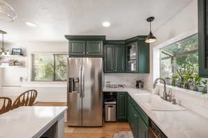 Kitchen with stainless steel refrigerator with ice dispenser, decorative light fixtures, sink, and a wealth of natural light