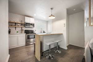 Kitchen featuring white cabinets, kitchen peninsula, a kitchen bar, hanging light fixtures, and appliances with stainless steel finishes