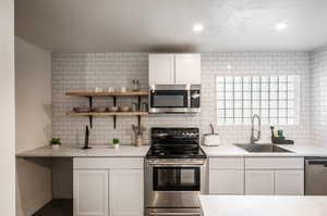 Kitchen with light stone counters, sink, white cabinetry, decorative backsplash, and appliances with stainless steel finishes