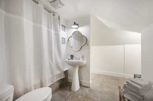 Bathroom featuring a textured ceiling, lofted ceiling, and toilet