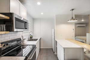 Kitchen featuring white refrigerator, black range with electric stovetop, sink, white cabinetry, and a wall mounted air conditioner