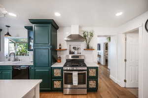 Kitchen featuring dishwasher, light hardwood / wood-style floors, sink, stainless steel gas range oven, and wall chimney exhaust hood