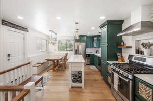 Kitchen with light wood-type flooring, wall chimney exhaust hood, stainless steel appliances, and tasteful backsplash