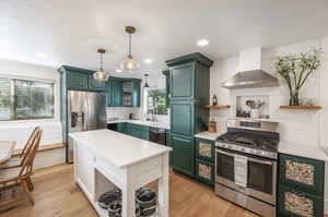 Kitchen featuring decorative light fixtures, stainless steel appliances, light wood-type flooring, and wall chimney range hood