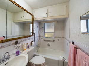 Full bathroom with tile walls, toilet, sink, and tiled shower / bath