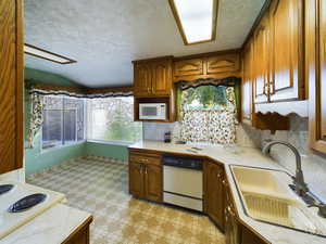 Kitchen featuring vaulted ceiling, dishwasher, sink, and a textured ceiling