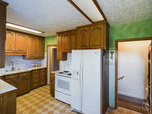 Kitchen with a textured ceiling, white appliances, and sink