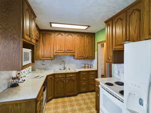 Kitchen with white appliances, a textured ceiling, and sink