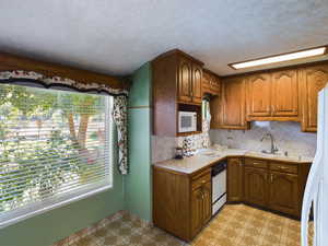 Kitchen featuring a textured ceiling, decorative backsplash, white appliances, and sink