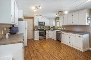 Kitchen with sink, stainless steel appliances, dark wood-type flooring, and white cabinetry