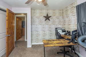 Office area featuring a textured ceiling, carpet flooring, wood walls, and ceiling fan