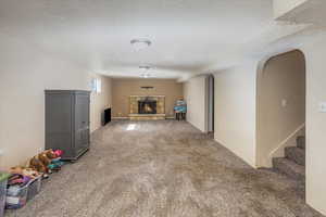 Rec room featuring a textured ceiling, carpet, and a stone fireplace