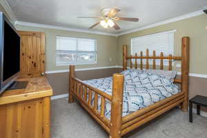 Carpeted bedroom with ceiling fan and crown molding