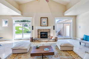 Living room featuring a stone fireplace, ceiling fan, tile patterned floors, and high vaulted ceiling