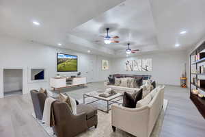 Living room with light hardwood / wood-style flooring, a tray ceiling, and ceiling fan