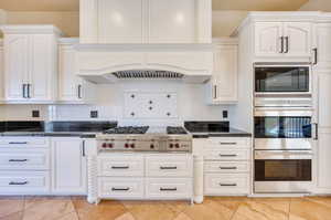 Kitchen with white cabinetry, custom exhaust hood, decorative backsplash, stainless steel appliances, and light tile patterned floors