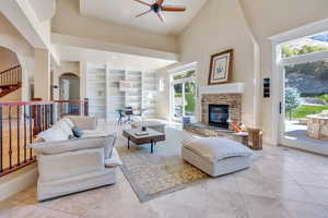 Tiled living room featuring high vaulted ceiling, ceiling fan, a fireplace, and a healthy amount of sunlight