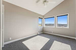 Carpeted empty room featuring ceiling fan and vaulted ceiling