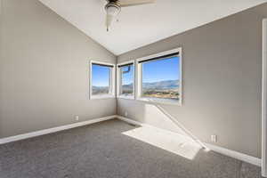 Carpeted spare room featuring a mountain view, ceiling fan, and lofted ceiling