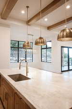 Kitchen with light stone countertops, beam ceiling, sink, and pendant lighting