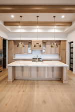 Kitchen featuring pendant lighting, beamed ceiling, light wood-type flooring, and a large island with sink