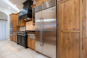 Kitchen with light tile patterned floors, appliances with stainless steel finishes, backsplash, and custom range hood