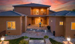 Back of house at dusk with a patio, a balcony, stucco siding, and a tiled roof